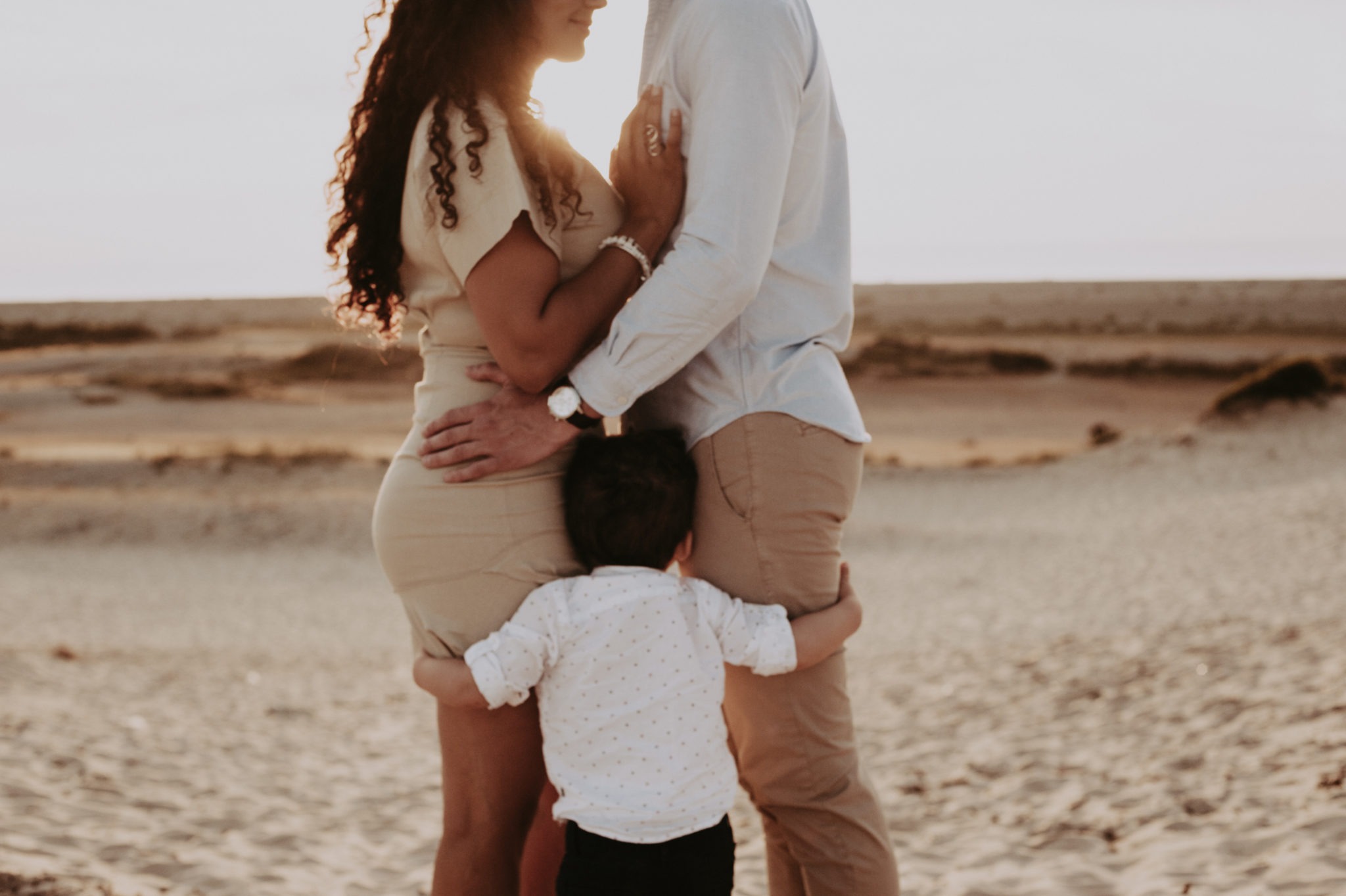 Séance photo en famille en Dordogne avec les deux parents en tête à tête et leur petit garçon à leurs pieds au couché du soleil