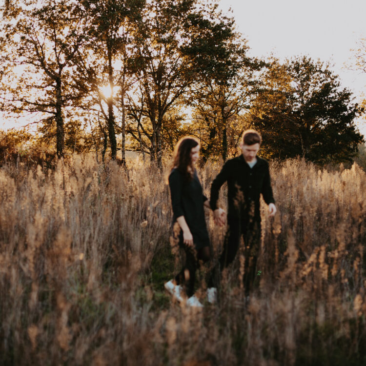 couple qui marche dans les herbes haute au couché de soleil