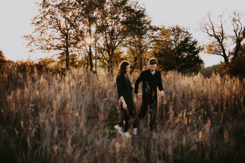 couple qui marche dans les herbes haute au couché de soleil