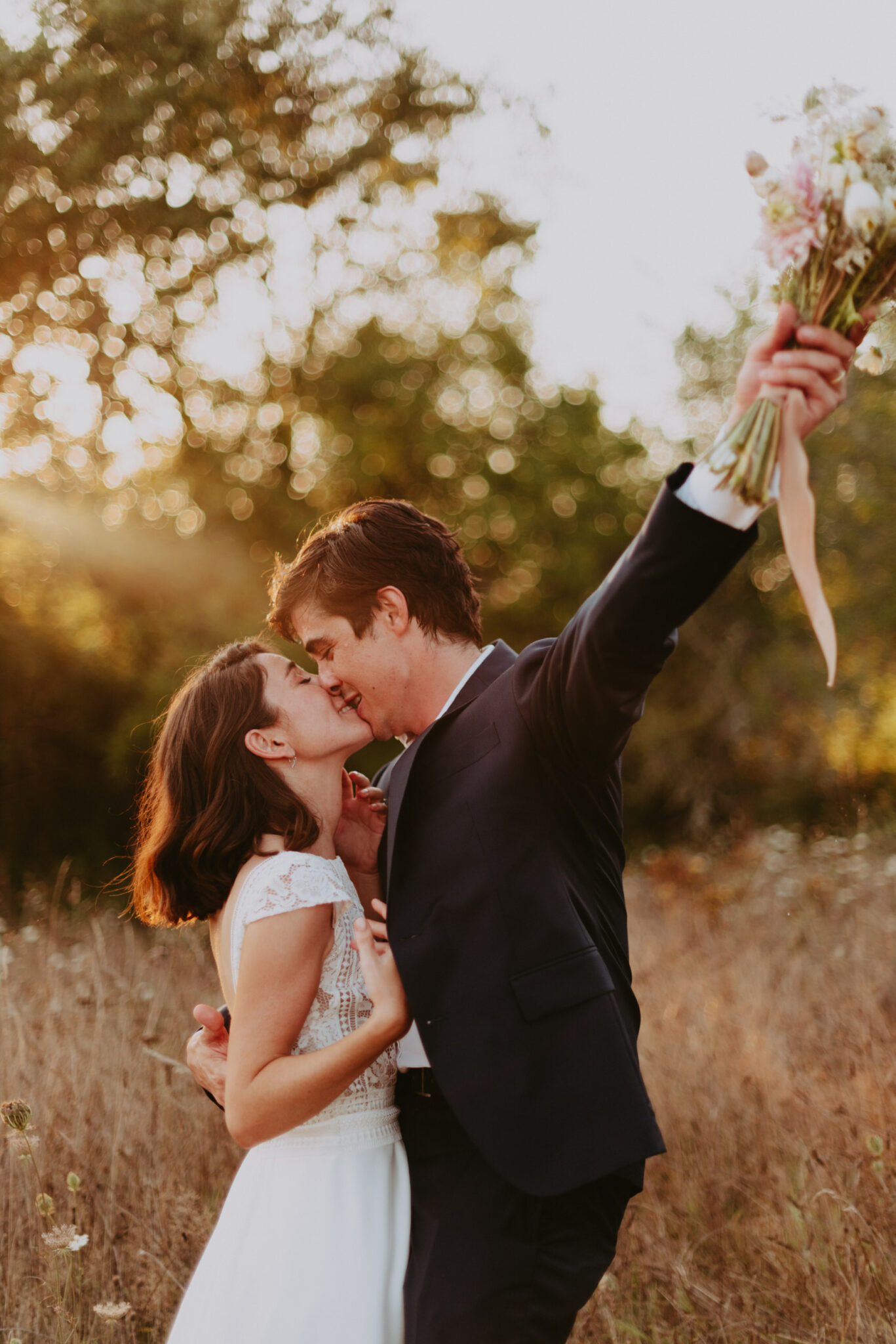 un couple de jeune marié s'embrasse tendrement dans un champ au coucher de soleil