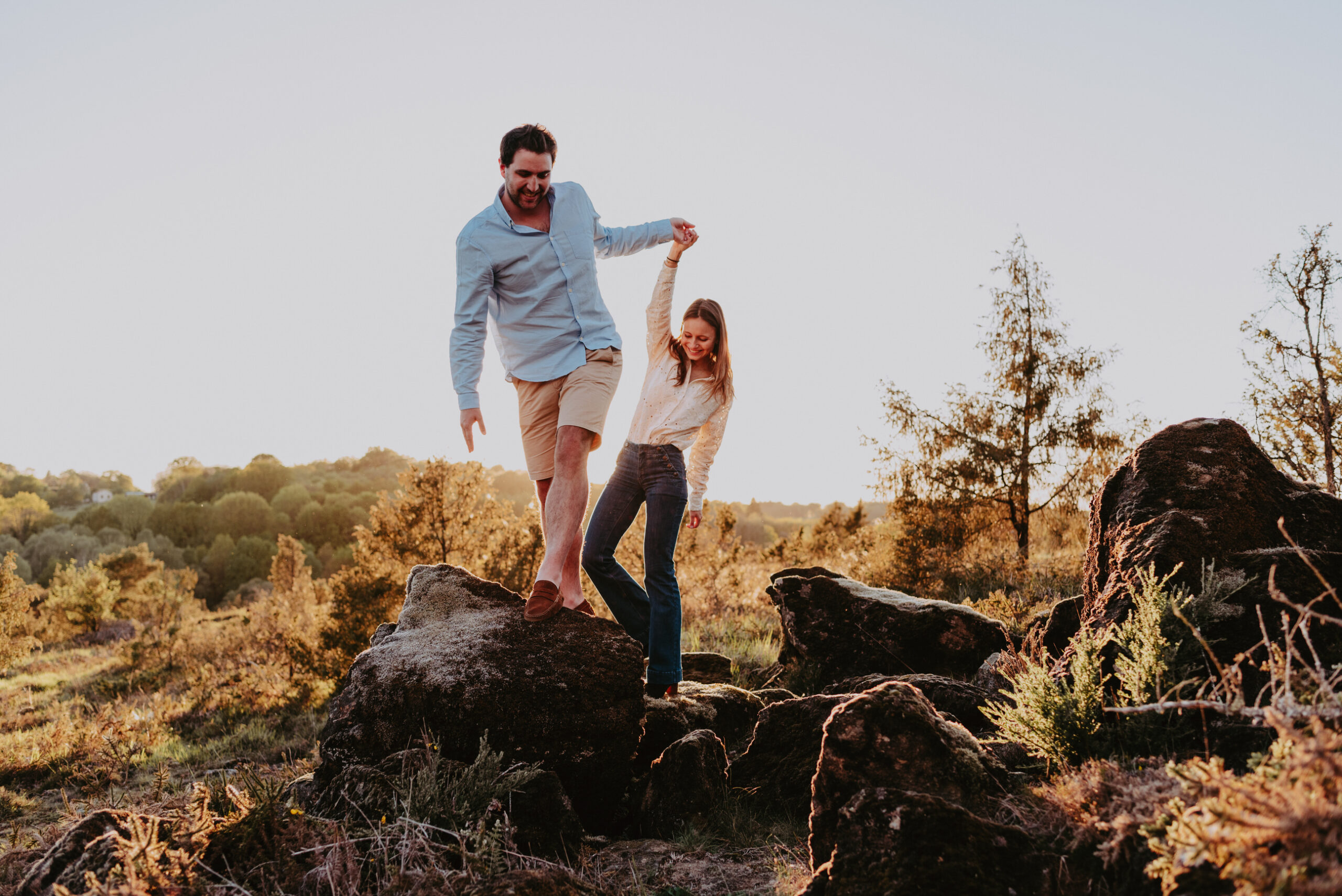 couple qui s'embrasse débout sur un rocher au couché de soleil