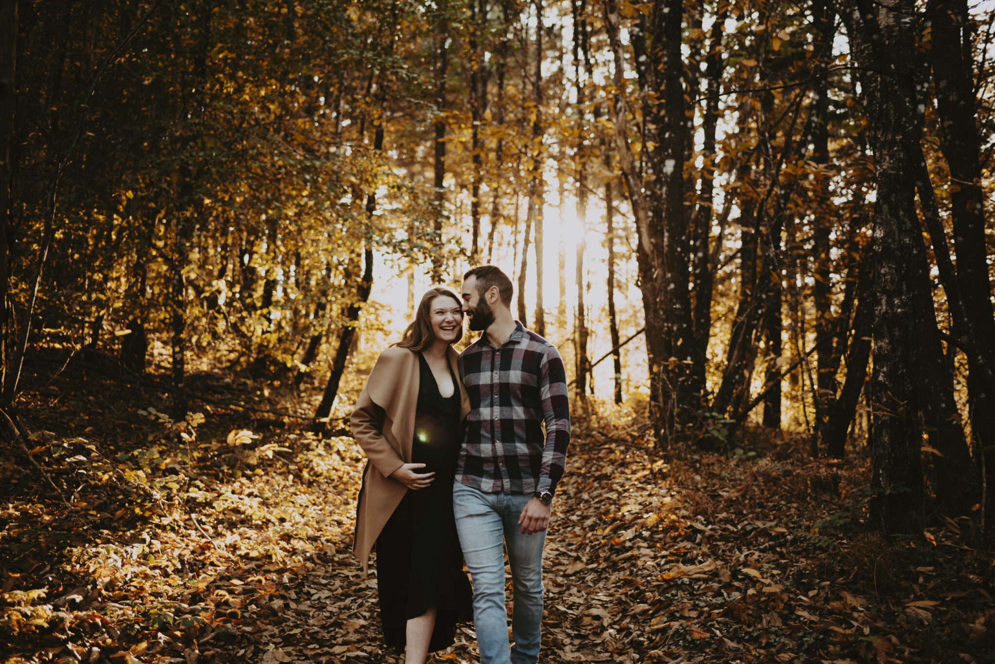 photo d'une femme enceinte avec son conjoint qui marche en riant en forêt
