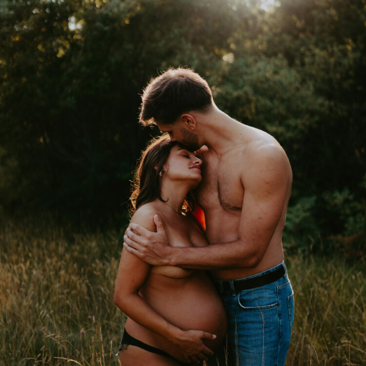 photo d'une femme enceinte de de son conjoint torse nu dans un champ