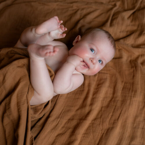 photo d'un bébé sur le dos qui mange sa main et sourie