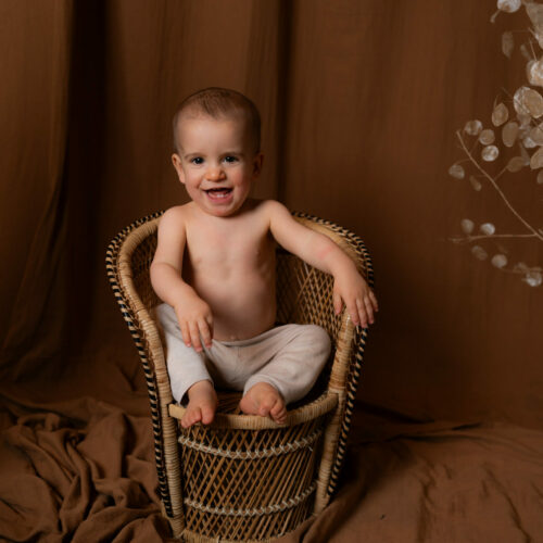 photo bébé assis sur une chaise en rotin qui rigole